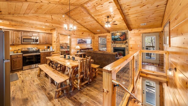 A log cabin interior with a kitchen, dining area, and a stone fireplace.