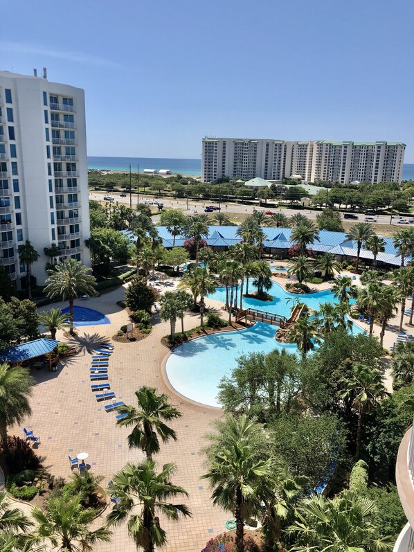 A resort with a large swimming pool, palm trees, and a view of the ocean. -  Destin's Salty Beach Paradise! (Destin)