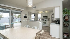 A modern kitchen with white cabinets, a central island, and a dining area with a large table and chairs. - Cliffrose pool home with RV/Boat parking (Lake Havasu City)