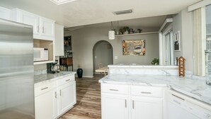 A modern kitchen with white cabinetry, a marble countertop, and a central island. - Cliffrose pool home with RV/Boat parking (Lake Havasu City)