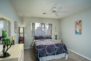 A bedroom with a bed, a ceiling fan, a window, a dresser, and a lamp.