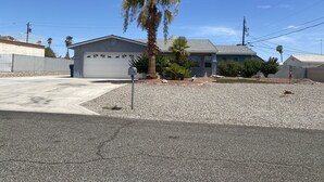 A residential house with a garage, a driveway, and a gravel front yard. - Cliffrose pool home with RV/Boat parking (Lake Havasu City)