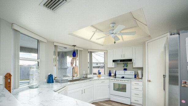 A modern kitchen with white cabinets, a marble countertop, a built-in oven, and a ceiling fan. - Cliffrose pool home with RV/Boat parking (Lake Havasu City)