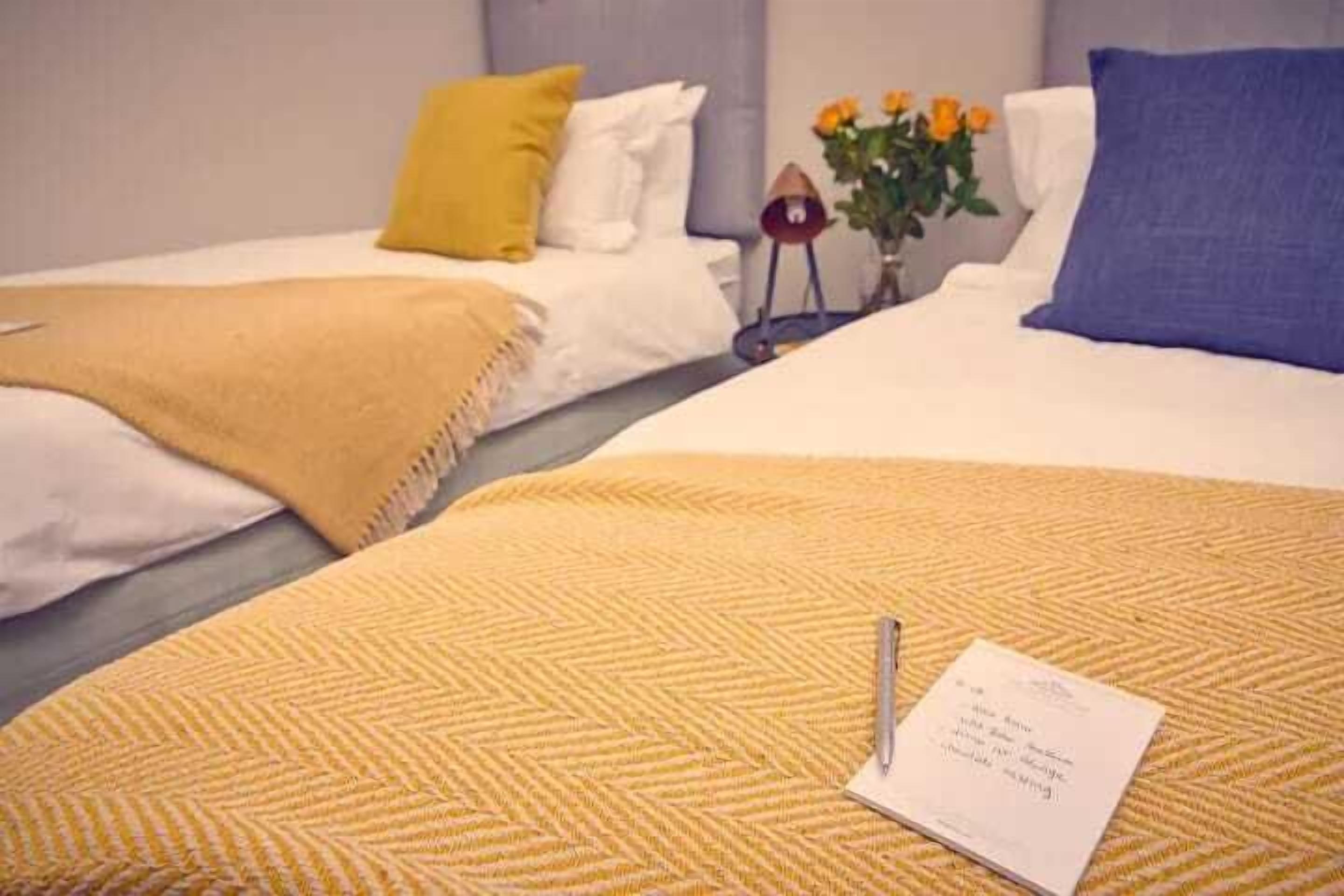 Habitación de hotel con dos camas, cada una con un edredón de color diferente, un jarrón con flores y una libreta en la cama.