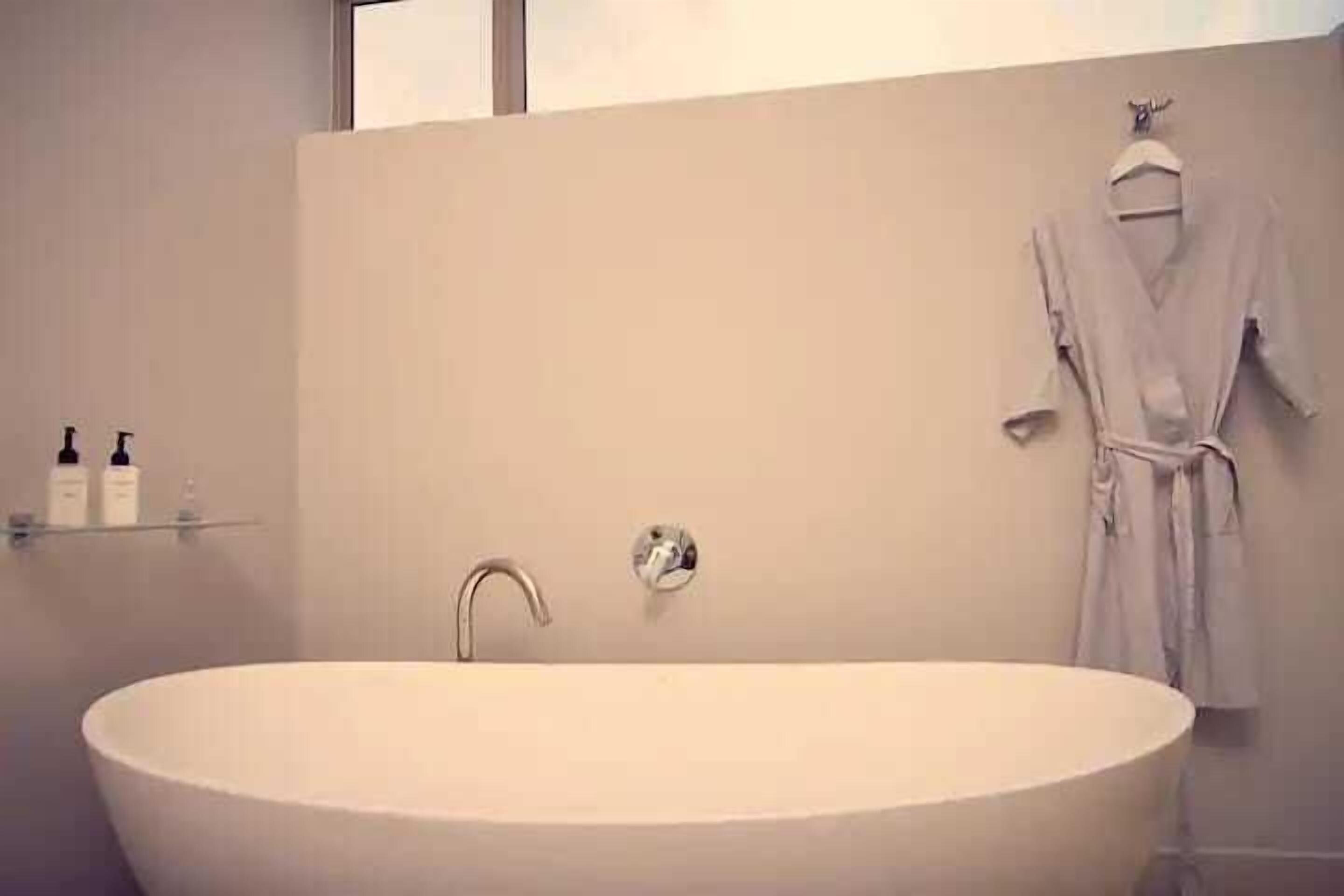A modern bathroom with a freestanding bathtub, a towel rack, and a shelf with toiletries.