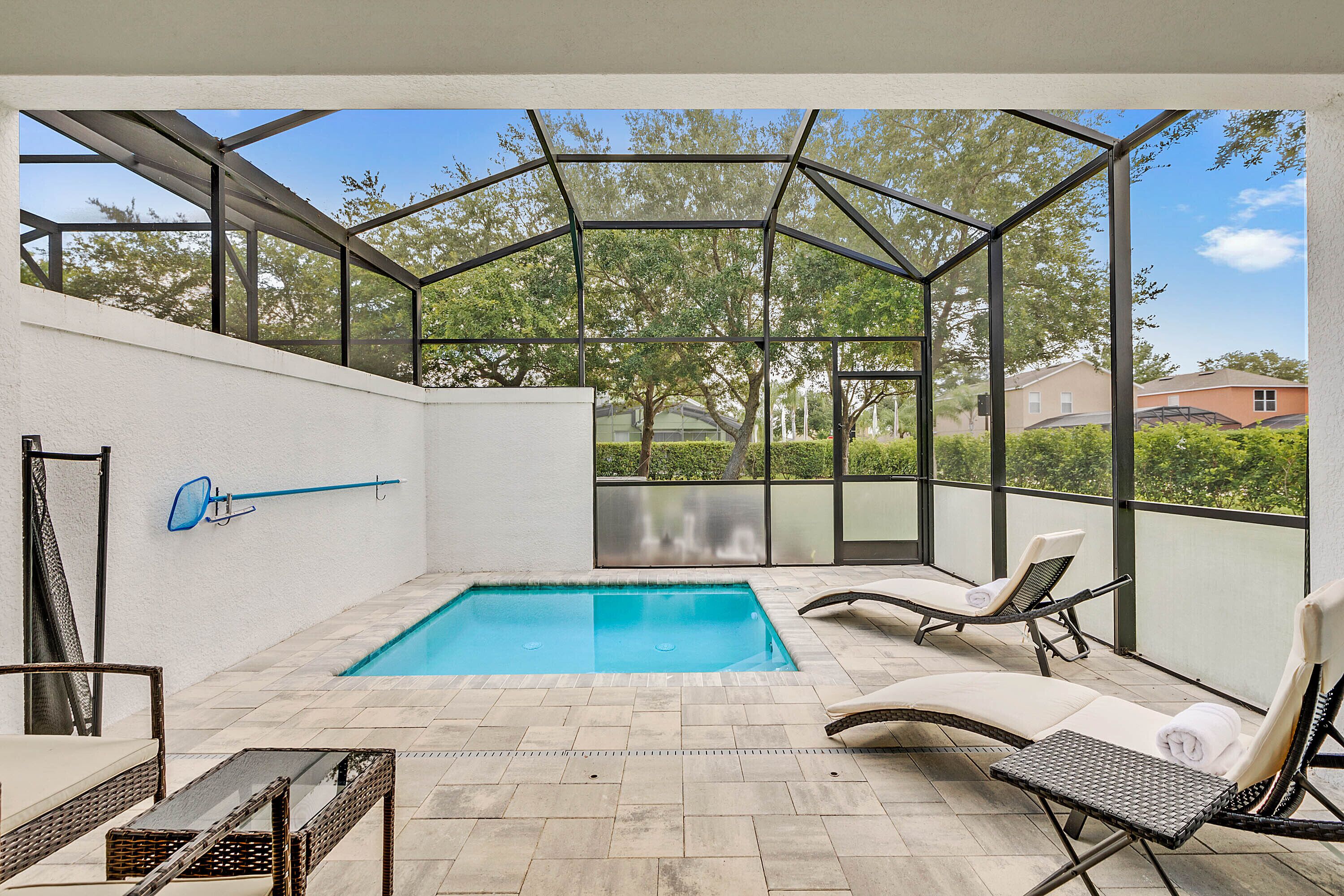 Une piscine extérieure couverte, dotée de chaises longues et d’une table, et entourée d’une structure en verre.