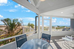 A covered outdoor area with a glass table and chairs, a view of the beach, and a white railing. - Sandals D | Luxury Beachfront Living on Sanibel Island (Sanibel)