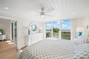 A bedroom with a large bed, a dresser, a vanity with a mirror, and a balcony with a view of the beach. - Sandals D | Luxury Beachfront Living on Sanibel Island (Sanibel)