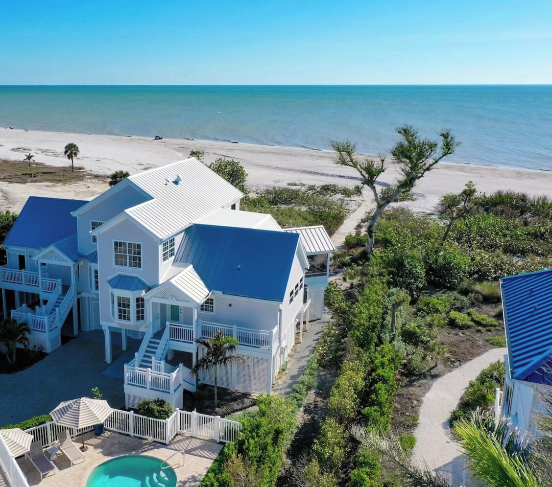 A large white house with a blue roof, a swimming pool, and a view of the beach.
