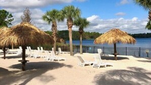 Une plage avec des chaises longues blanches et des parasols en chaume, des palmiers et un ciel bleu azur.
