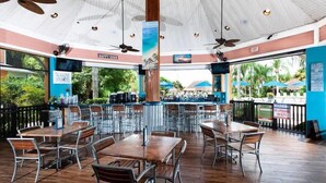 Un espace de restauration en plein air avec des tables et des chaises en bois, un comptoir de bar et une vue sur la plage.