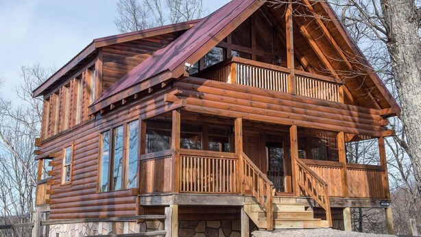 Eine Blockhütte mit Balkon, großen Fenstern und einem Steinfundament.