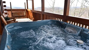 Ein Whirlpool mit Holzterrasse und Stühlen, umgeben von einem Geländer aus Holz mit Blick auf Bäume und Berge.
