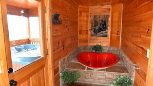 Ein Holzhütten-Interieur mit einer roten Badewanne, Steinstufen und einer Bärenplakette.