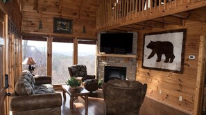 Cozy cabin with a seating area, stone fireplace, and large windows offering a scenic view.