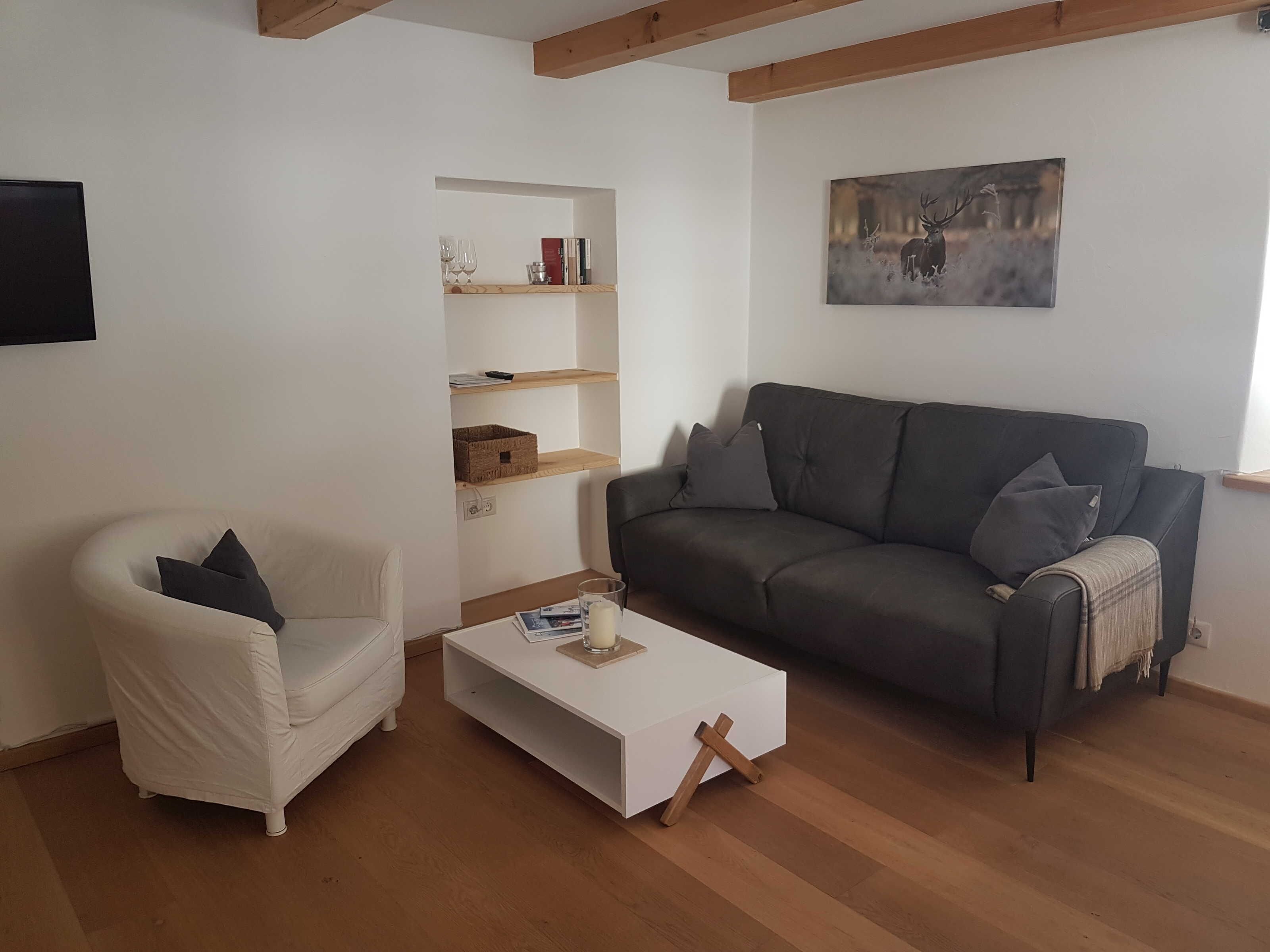 Un salón con un sillón blanco, un sofá gris, una mesita de centro blanca, estanterías de madera y un cuadro en la pared.
