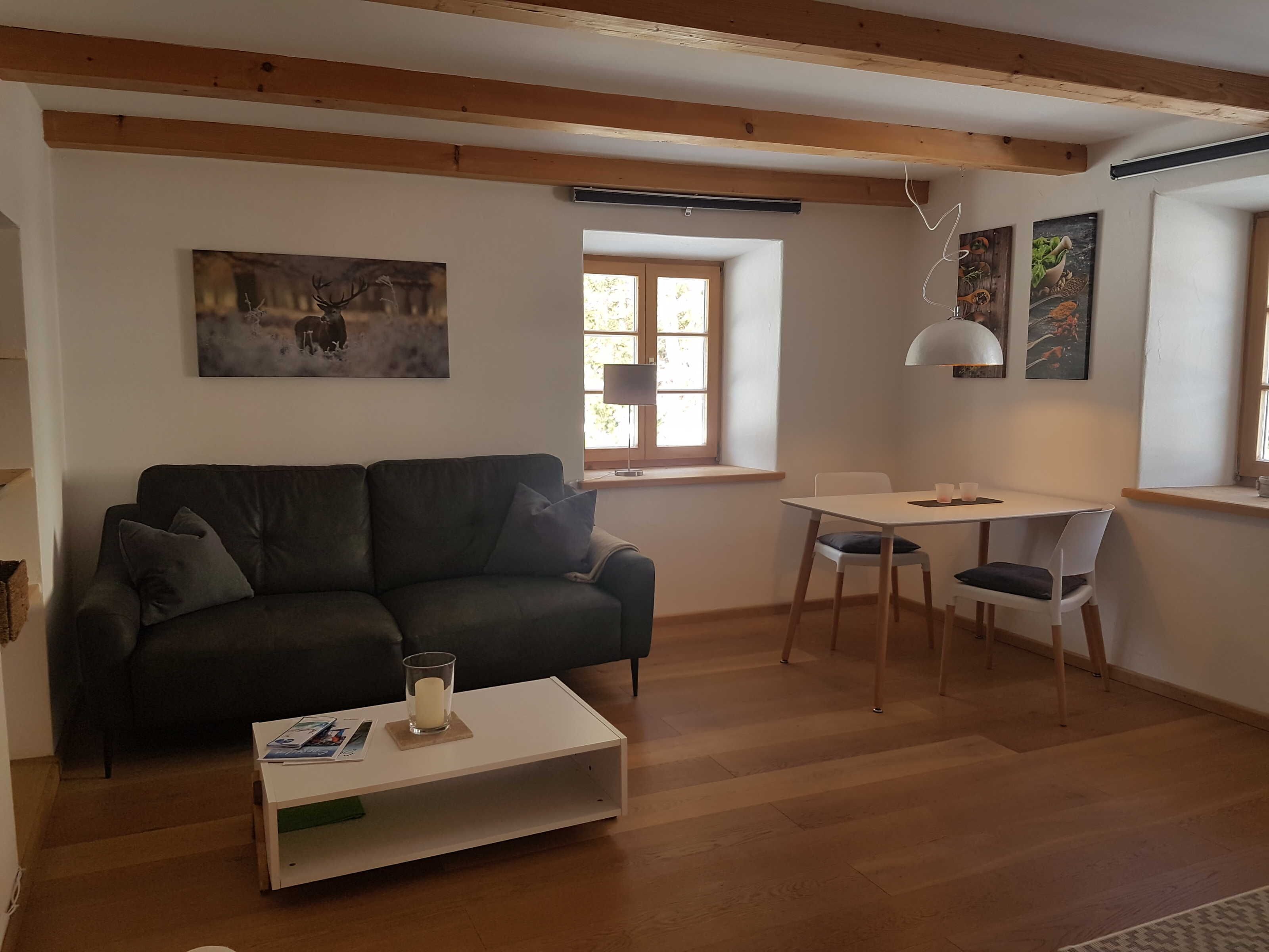 Un salón con un sofá verde oscuro, una mesa de centro blanca, una mesa de comedor con sillas y una ventana con vistas.