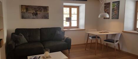 Un salón con un sofá verde oscuro, una mesa de centro blanca, una mesa de comedor con sillas y una ventana con vistas.