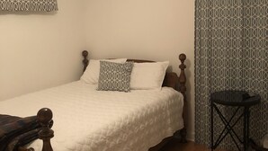 Une chambre à coucher avec un lit, un ventilateur de plafond, un rideau à motifs et une petite table.