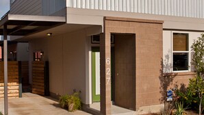 Un bâtiment doté d’un espace extérieur abrité, d’une porte verte et d’un mur en briques.