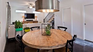 Un espace repas comprenant une table ronde en bois, des chaises noires et une lampe de table centrale avec un abat-jour en verre.