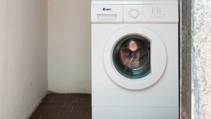 Ein kleiner Hauswirtschaftsraum mit einer weißen Waschmaschine, einem Holzregal darüber und einem gefliesten Boden.