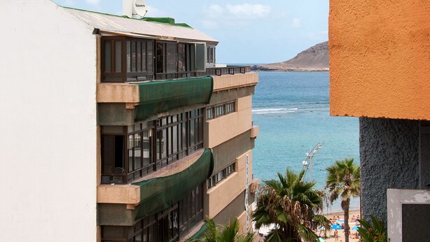 Ein mehrstöckiges Gebäude mit Balkonen, das auf einen Strand und das Meer blickt.