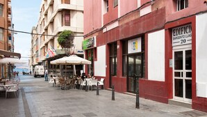 Eine Straße mit Außenbestuhlung, ein Gebäude mit dem Schild "EDIFICI SARGENTO LLAG 20" und ein geparkter Lastwagen.