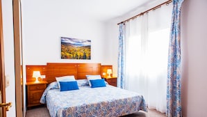 Ein Schlafzimmer mit einem Bett, einem Holzkopfende, Nachttischen, einer Lampe, einem Gemälde und gemusterten Vorhängen.