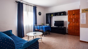 Ein Zimmer mit einem Bett, einem Esstisch mit Stühlen, einem Fernseher und einer Holztür.