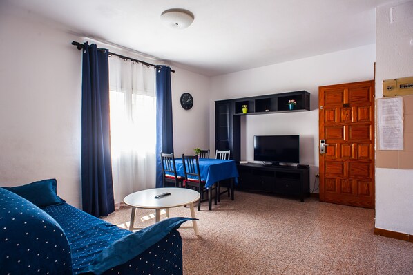 Una habitación con una cama, una mesa de comedor con sillas, un televisor y una puerta de madera.