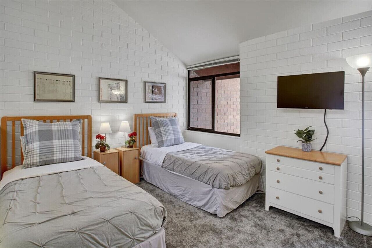 A bedroom with two beds, a TV, a bedside table with a lamp, and a dresser.