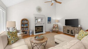 A living room with a fireplace, bookshelves, a television, and a ceiling fan.