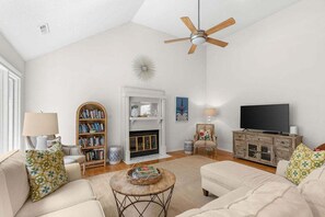 A living room with a fireplace, bookshelves, a television, and a ceiling fan.