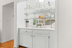 A white kitchen with a glass display shelf above the counter, holding various glassware and decorative items.