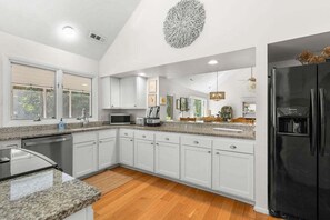 A modern kitchen with white cabinets, granite countertops, a black refrigerator, and a large decorative wall piece.