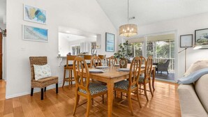 A dining area with a wooden table and chairs, a wicker chair, and artwork on the walls.