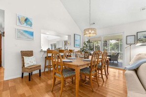 A dining area with a wooden table and chairs, a wicker chair, and artwork on the walls.