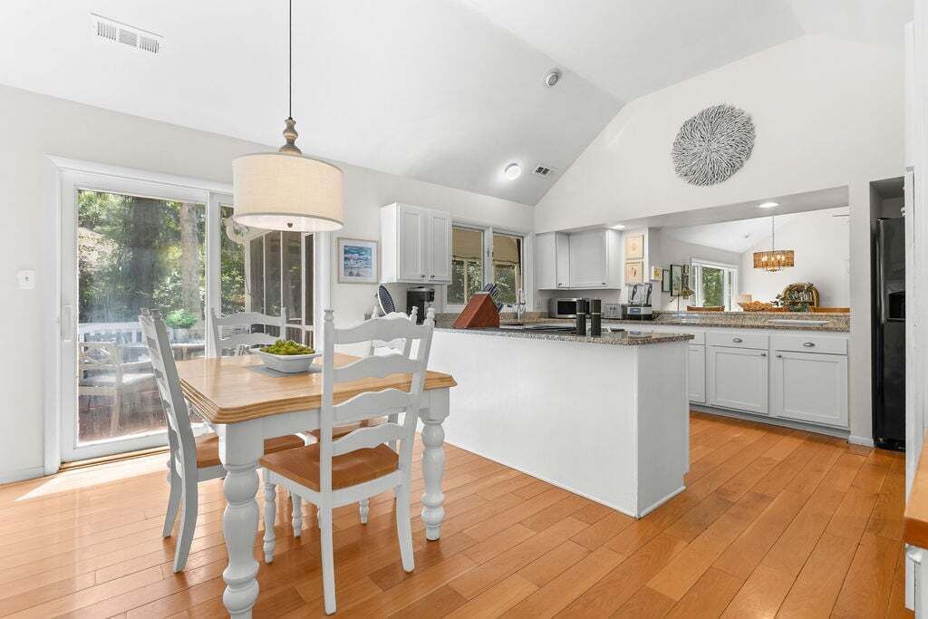 A spacious kitchen with a central island, white cabinetry, and a dining area with a table and chairs.