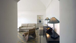 A living room with a sofa, a chair, a lamp, and a shelf with decorative items. - Nice apartment with private terrace. Shared pool. In Donnafugata, Sicily (Donnafugata)