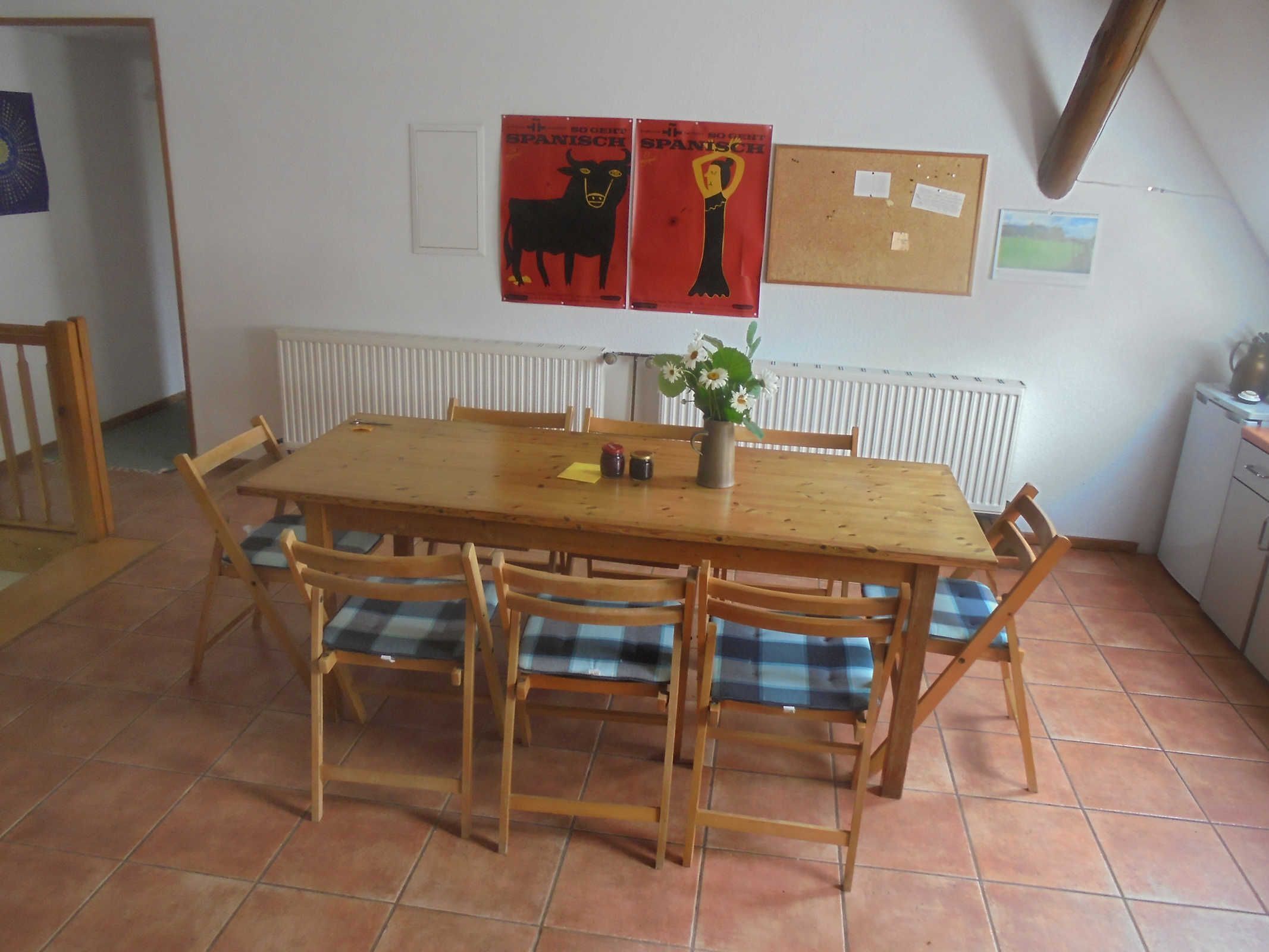 A dining area with a wooden table and chairs, a radiator, and two posters on the wall.