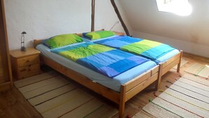 A single bed with a colorful quilt, a bedside table, a small lamp, and a window with a view of the outside. - Apartment - For Güstrow: Apartment Bergfeld (Lalendorf)