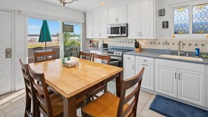 A kitchen with white cabinets, a wooden dining table, and a view of the outdoors. - Bayfront with great patio! (San Diego)