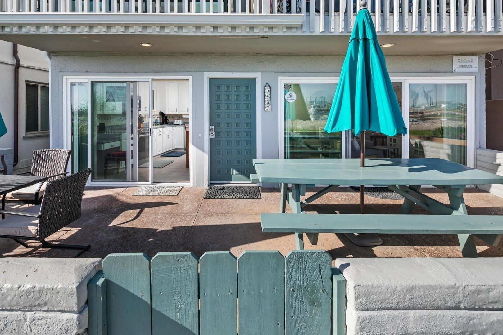 A beach house with a patio area featuring a table and chairs, a covered seating area, and a sliding glass door leading to a kitchen.