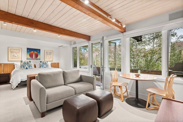 A modern interior with a bed, sofa, ottoman, and a dining area with chairs and a table.