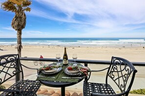 A table set for two with a bottle of wine and glasses, overlooking a beach with the ocean and a palm tree. - Two bedroom on the ocean front. (San Diego)