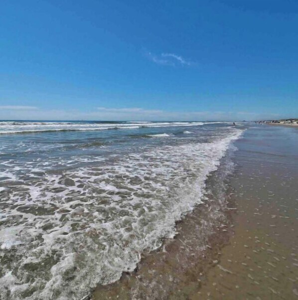 A beach with waves reaching the shore, a clear sky, and distant buildings. - 33❤️Waterfront❤️Fishing Dock❤️Close to beach❤️King Bed (BreckenridgeCorpus Christi)