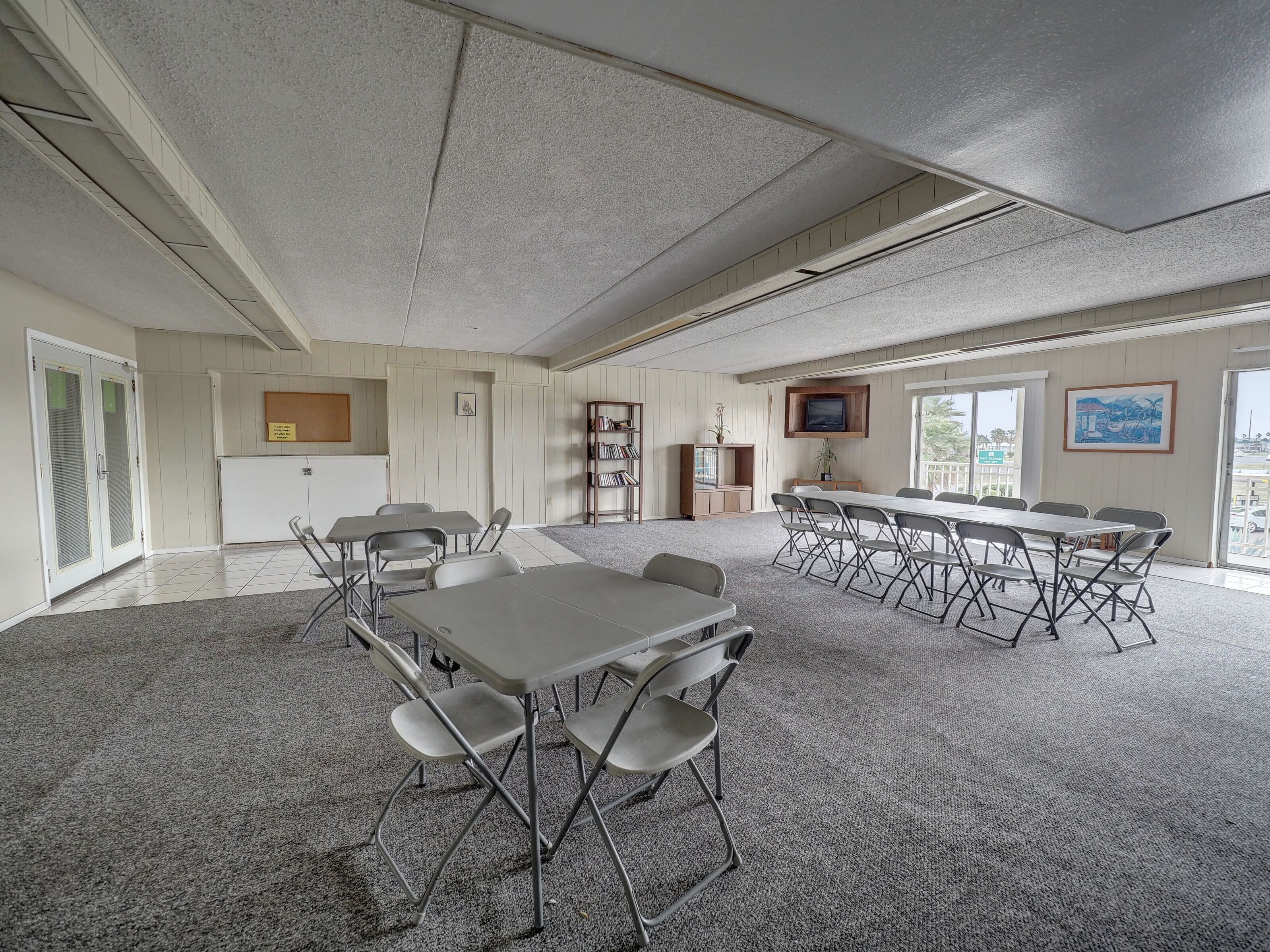 A spacious conference room with a large table and chairs, carpeted floor, and a television mounted on the wall.