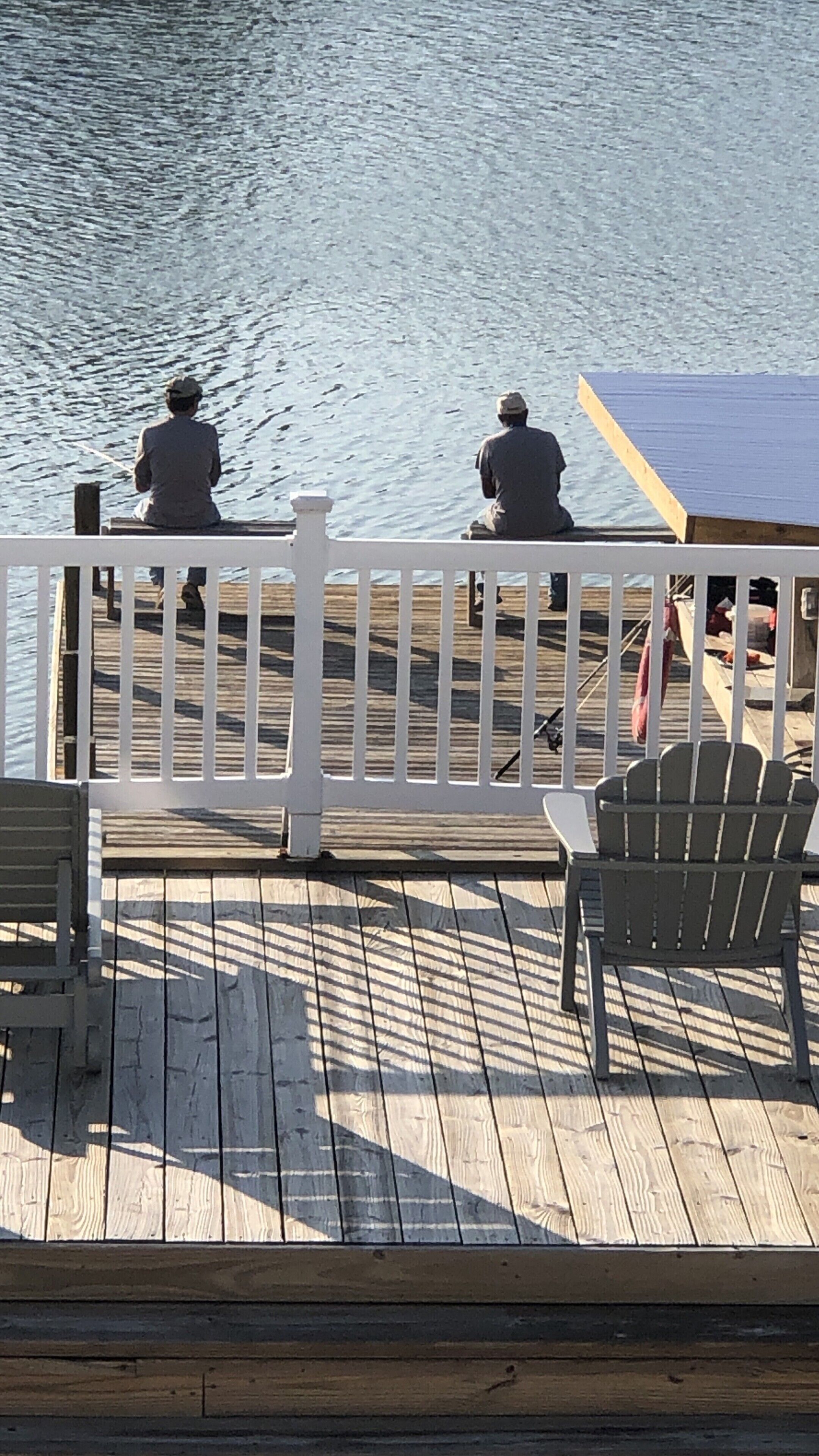 A wooden pier with two people sitting on benches, overlooking a body of water.
