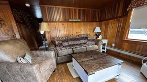 Un salon chaleureux avec un canapé en cuir marron, un divan à motifs et une table basse en bois.